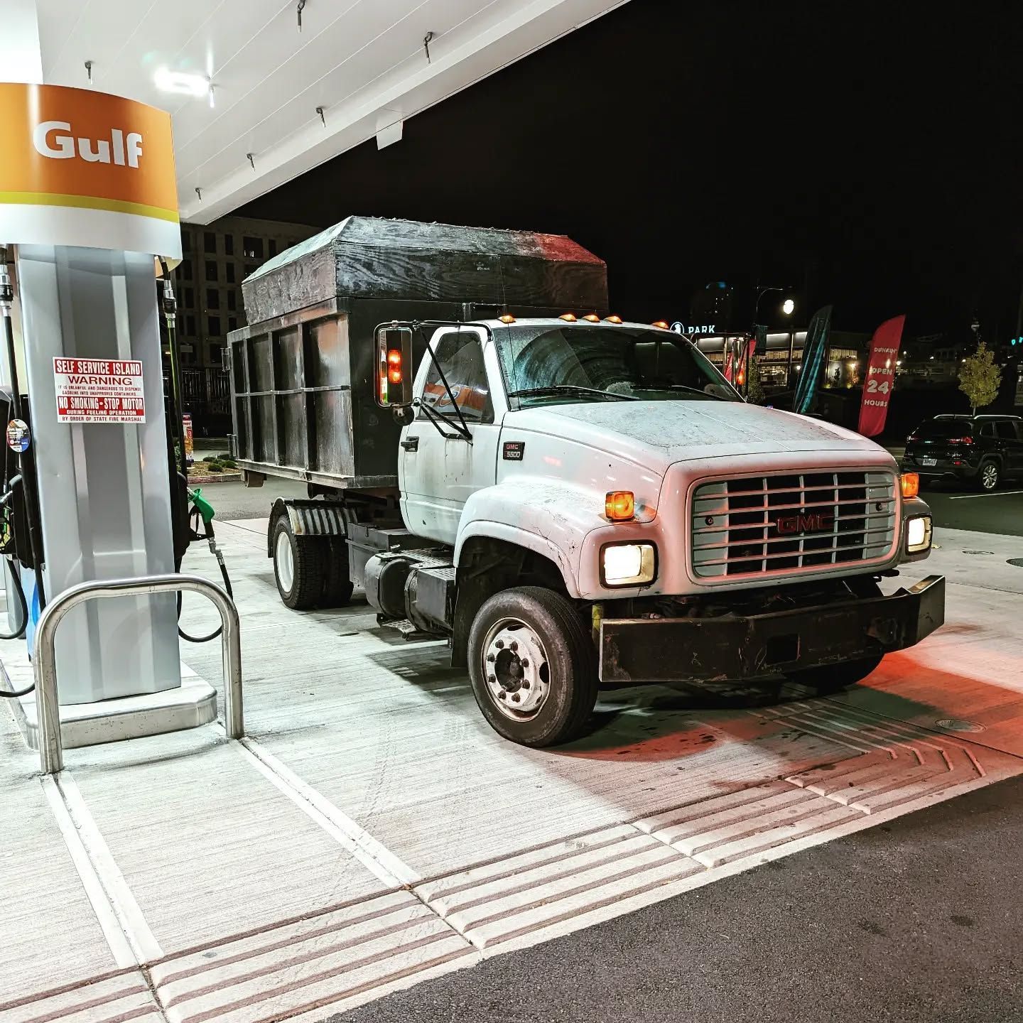 A white dump truck at a Gulf gas station at night, parked at a pump.