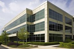 Modern three-story office building with large windows, beige exterior, and manicured landscaping.