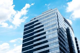 Modern glass skyscraper against a blue sky with scattered clouds.