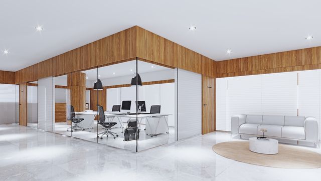 Modern office with glass-walled workspaces, wooden accents, white furniture, and a waiting area with a sofa.