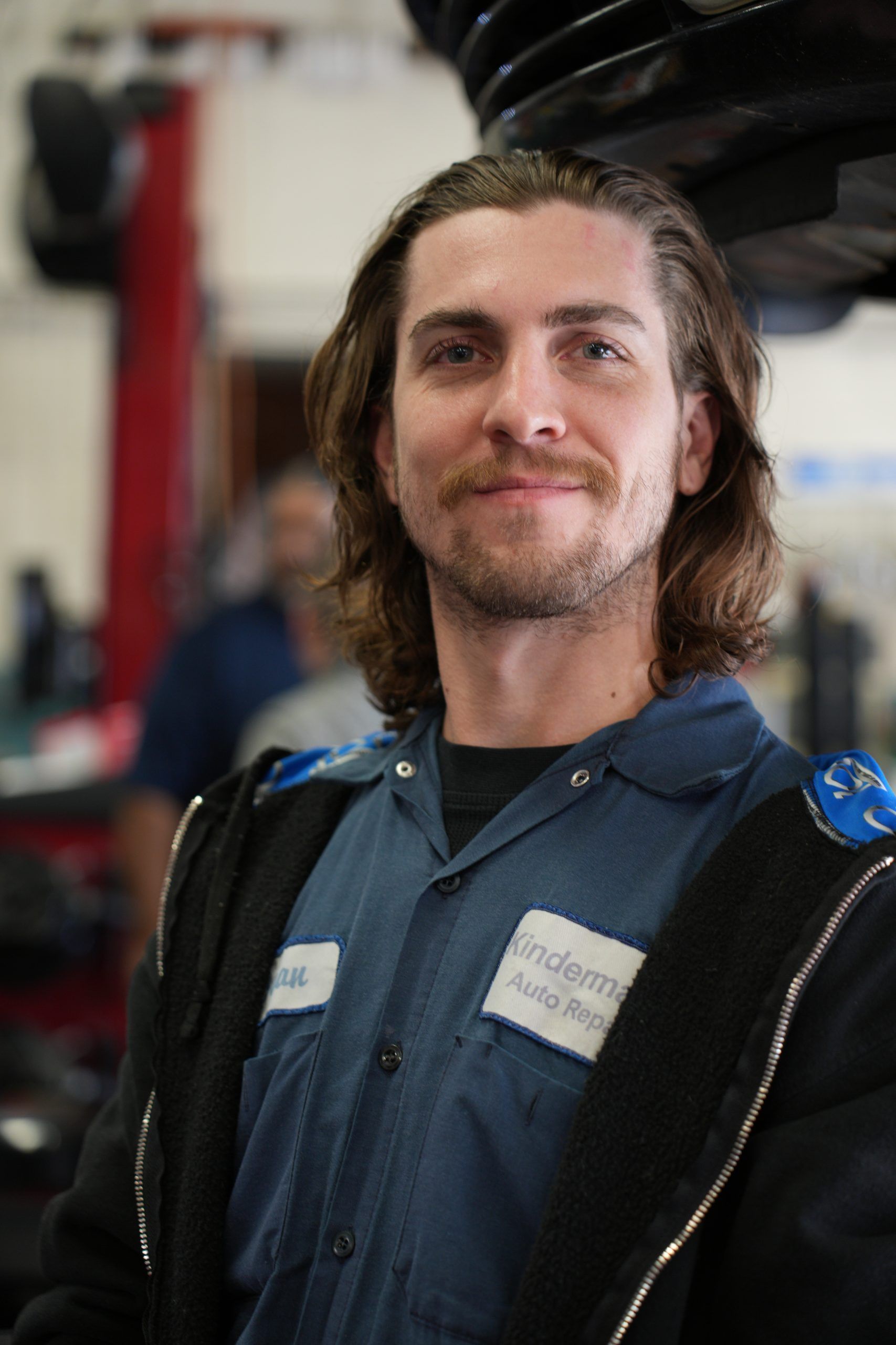 Person in a blue work shirt and black jacket smiling in a workshop.