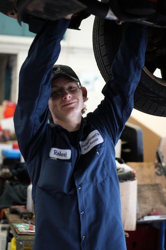 Mechanic in blue coveralls working under a car on a lift in an auto shop