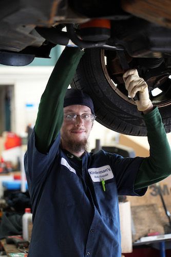 Mechanic in blue coveralls working under a raised car in an auto shop