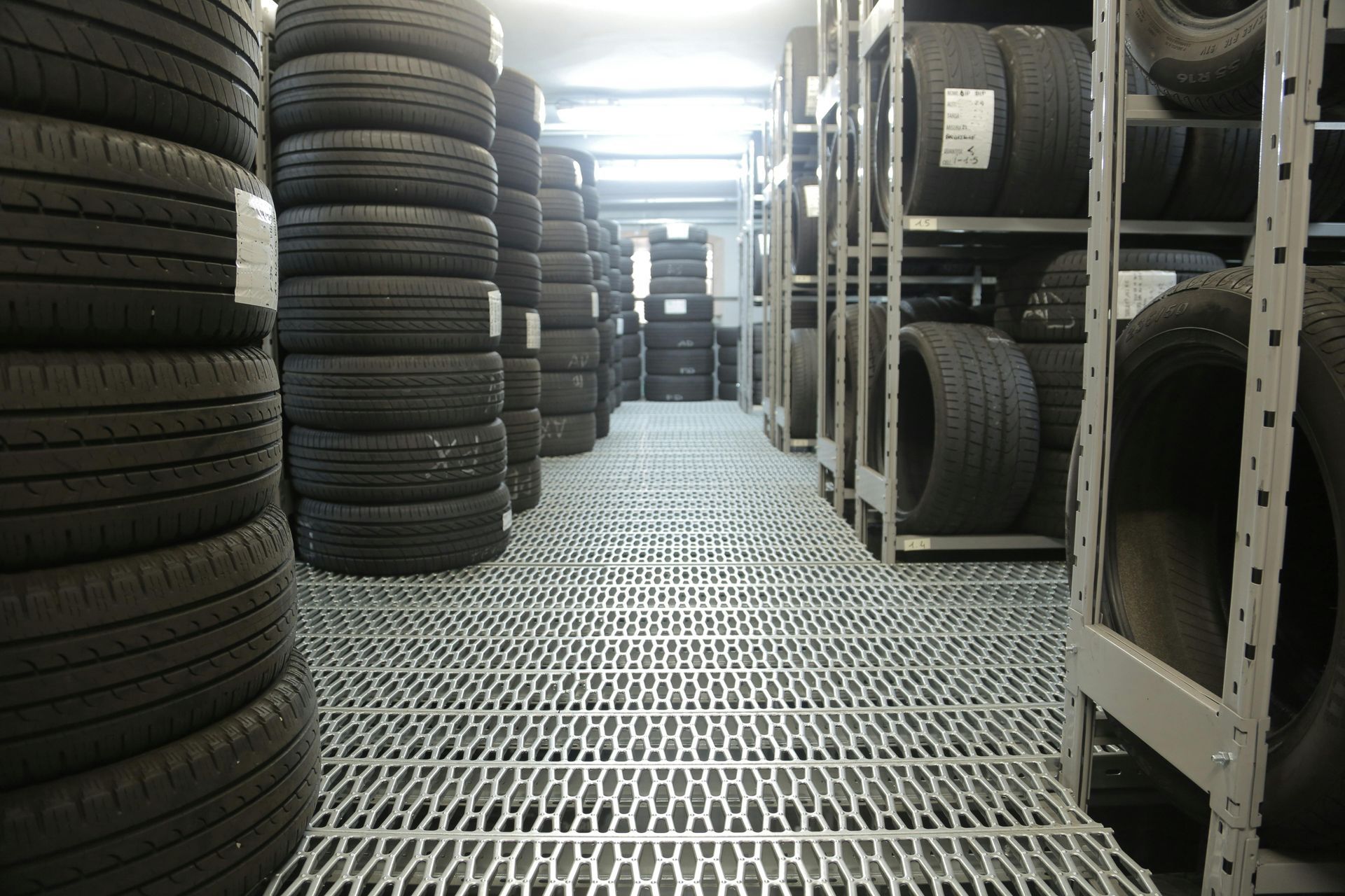 Rows of stacked black tires on metal shelving in a warehouse aisle
