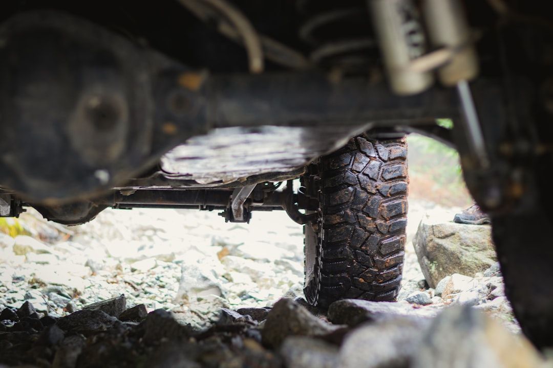 Close-up of a rugged off-road tire and suspension under a vehicle on rocky ground