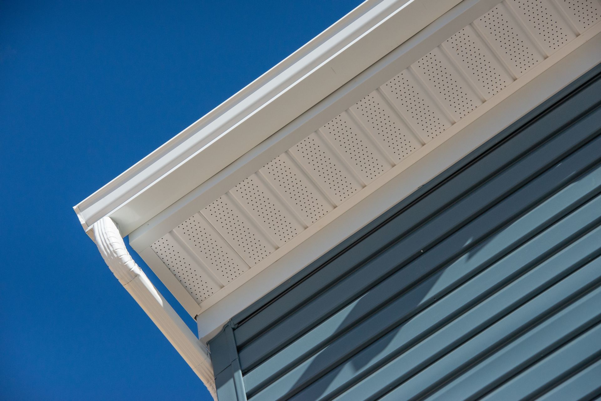 White house eaves with vented soffit against a clear blue sky