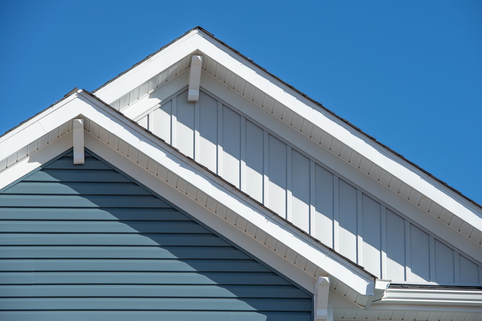 Brick house with gray shingle roof and four vents against a blue sky
