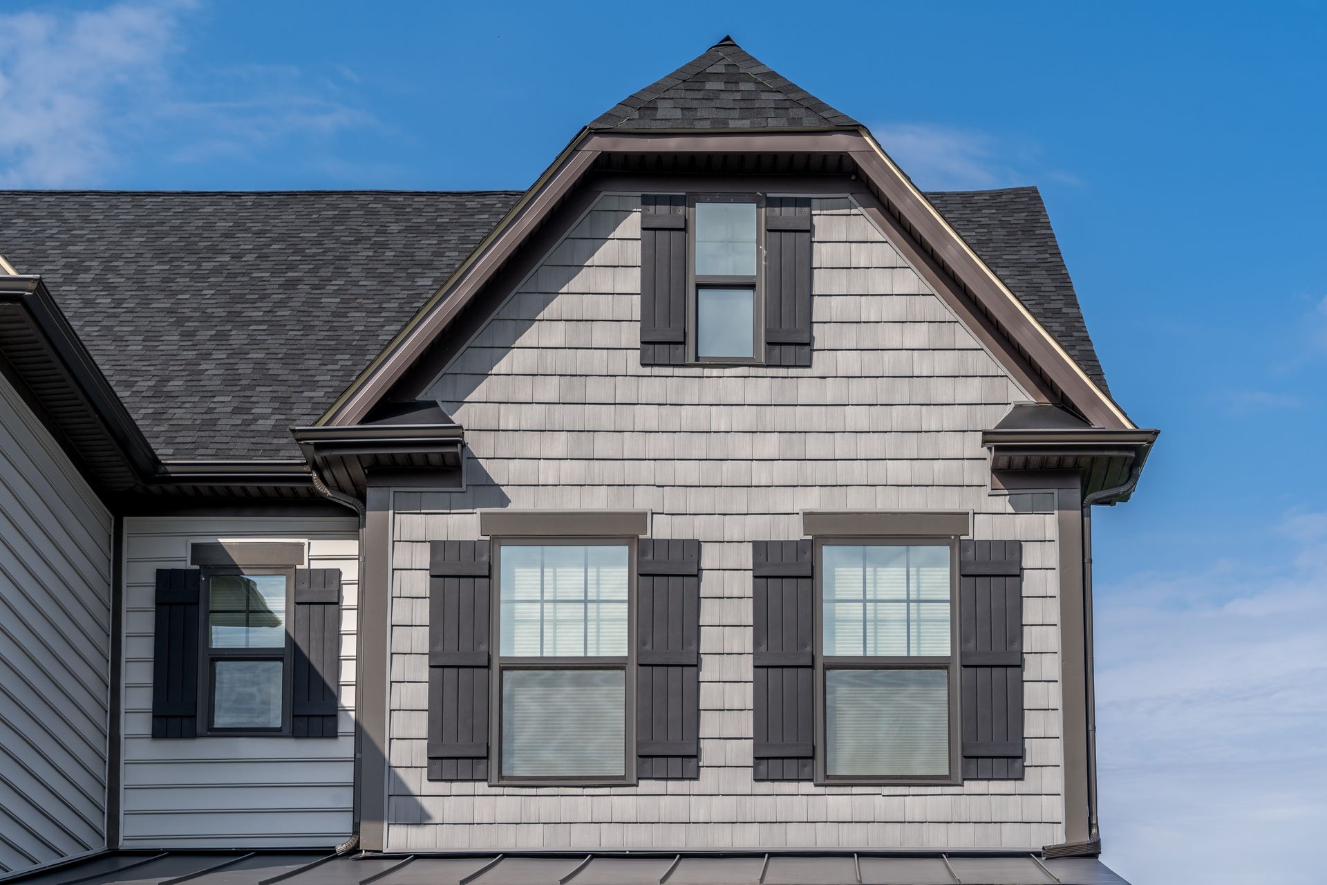 Gray house exterior with dark shutters and a blue sky backdrop