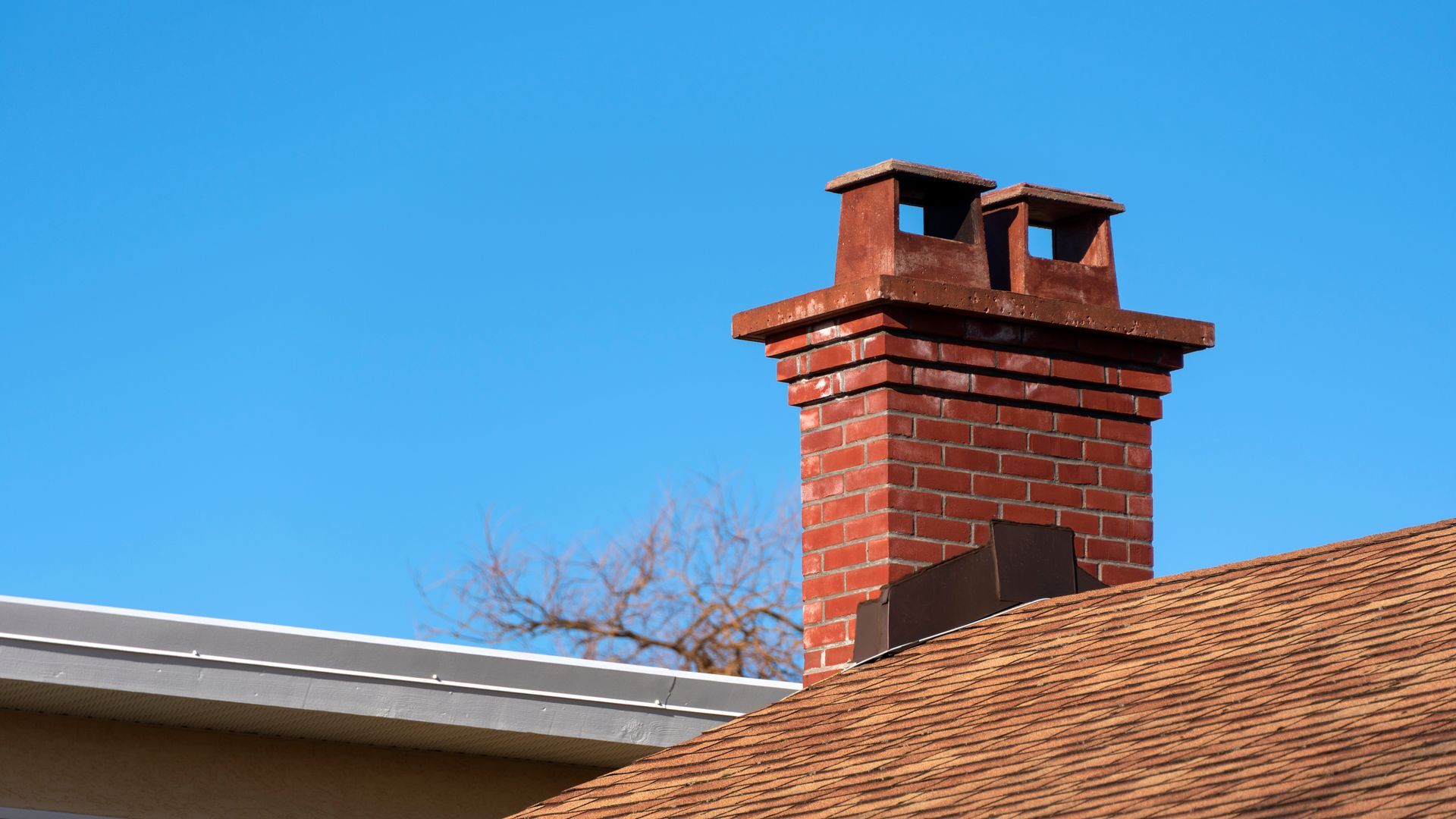 Brick chimney with two flues on a house roof against a clear blue sky