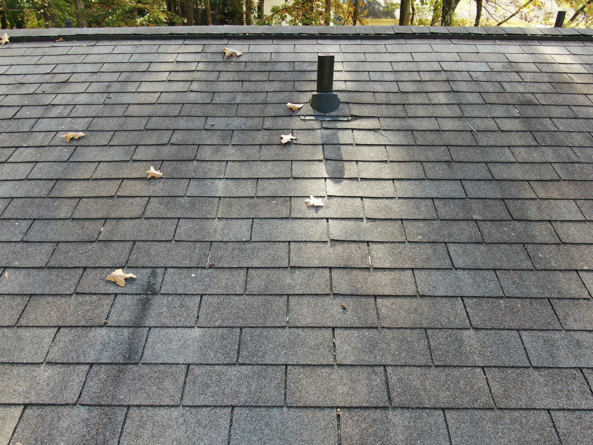 Brick house with gray shingle roof and four vents against a blue sky