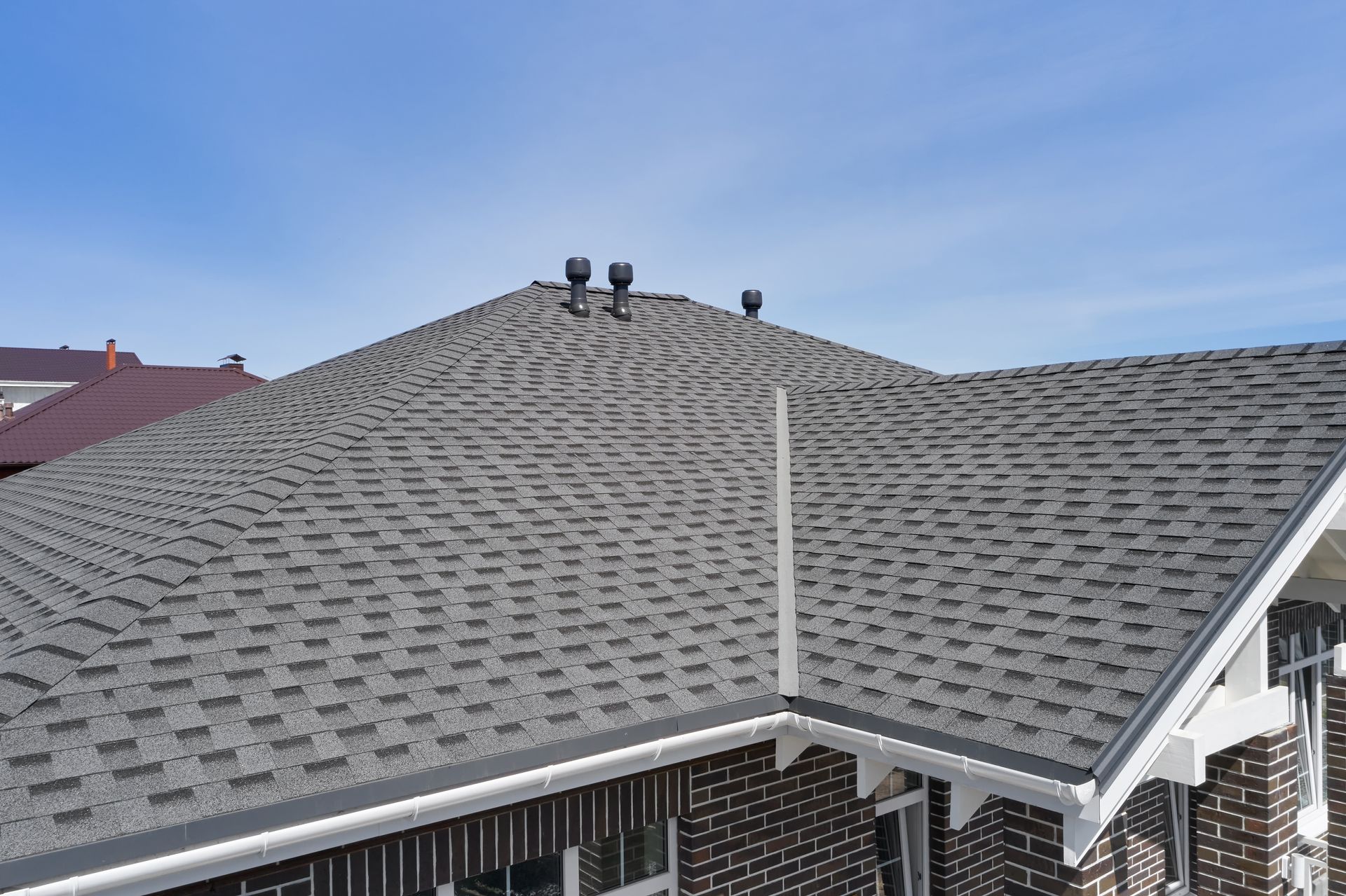 Hands use a utility knife to cut black roofing material on a flat surface.