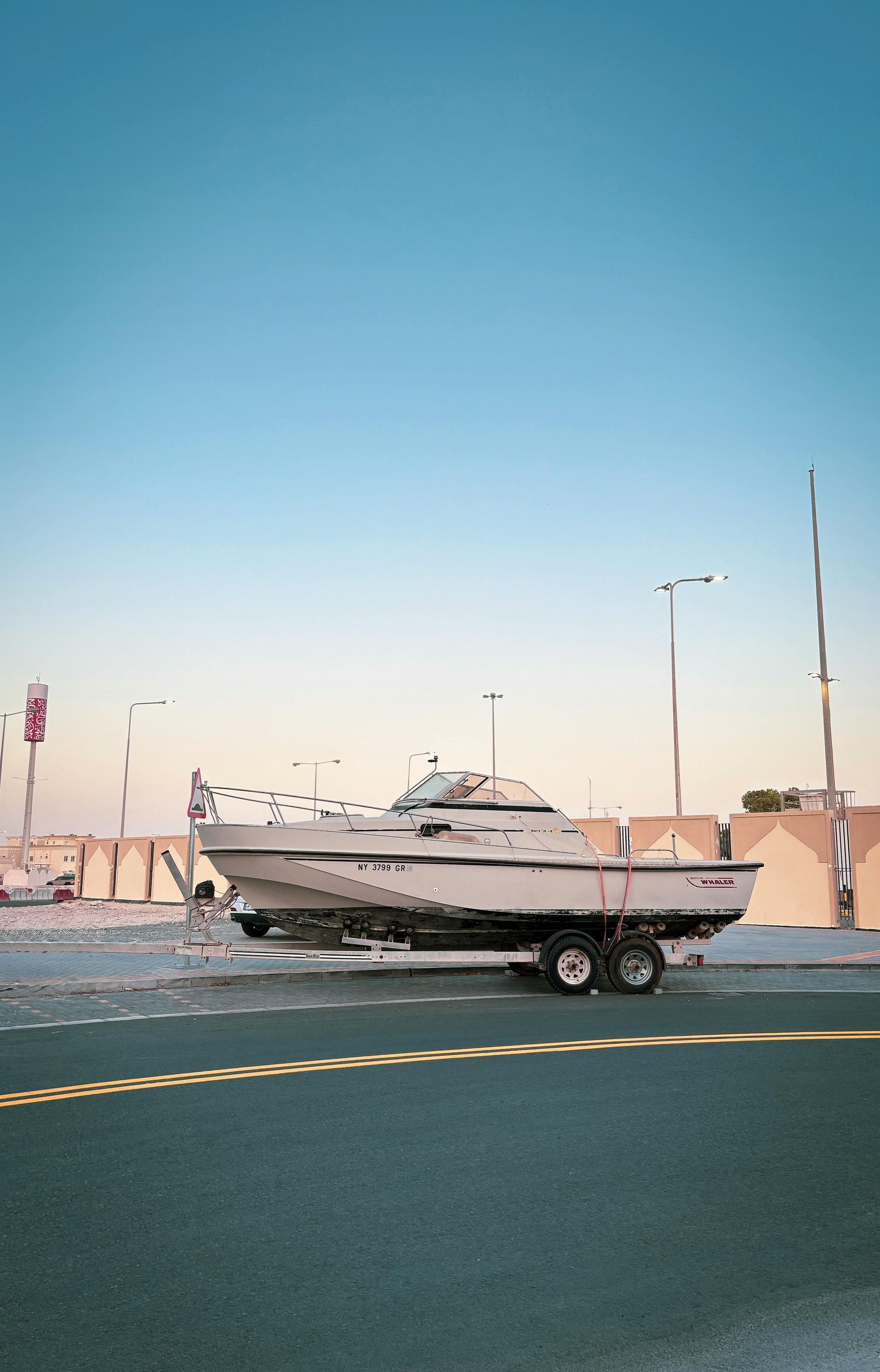 A boat is on a trailer on the side of a road.