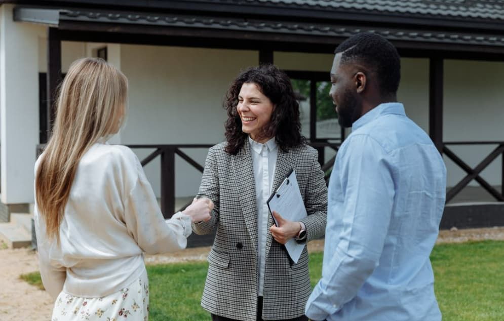 A man and a woman are standing in front of a house talking to a real estate agent.