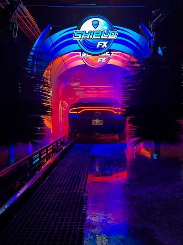 A car moving through a neon-lit, futuristic car wash tunnel with a