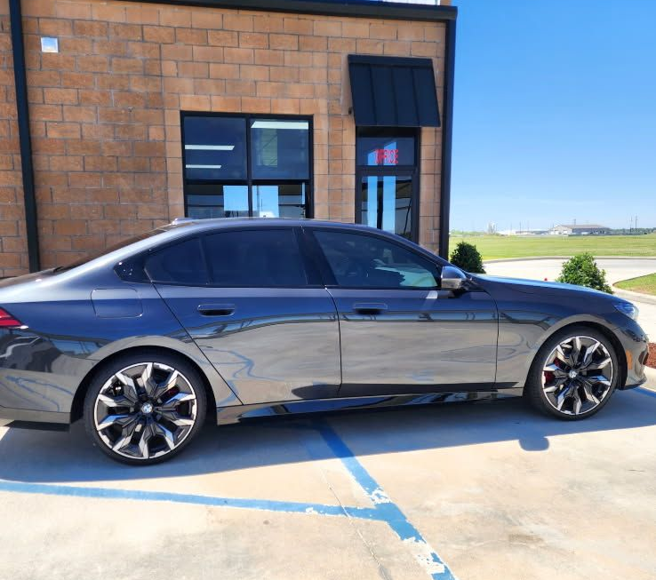 A dark gray sedan parked in a concrete lot next to a brick building on a sunny day.