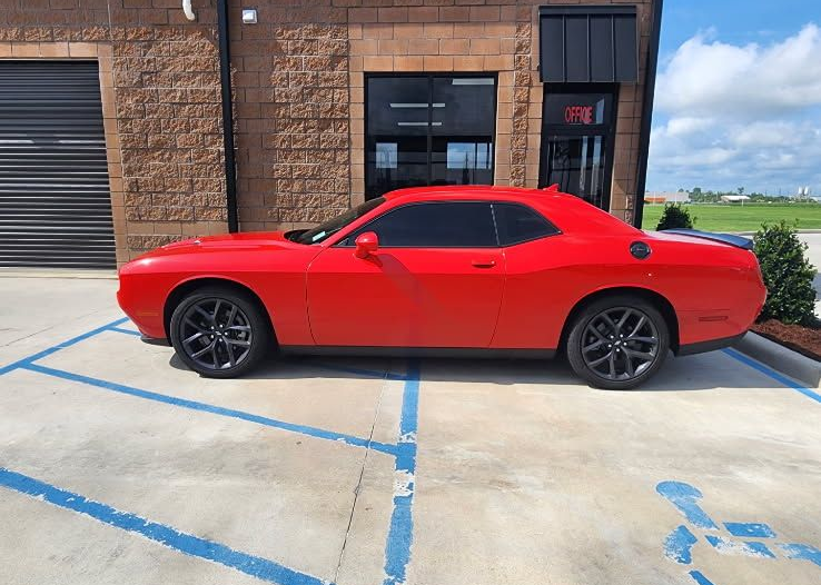 A bright red Dodge Challenger coupe parked in a designated handicap spot in front of a brick commercial building.