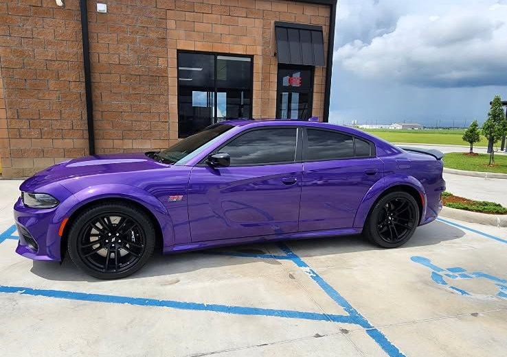 A vibrant purple Dodge Charger parked in a handicapped spot outside a brick building.