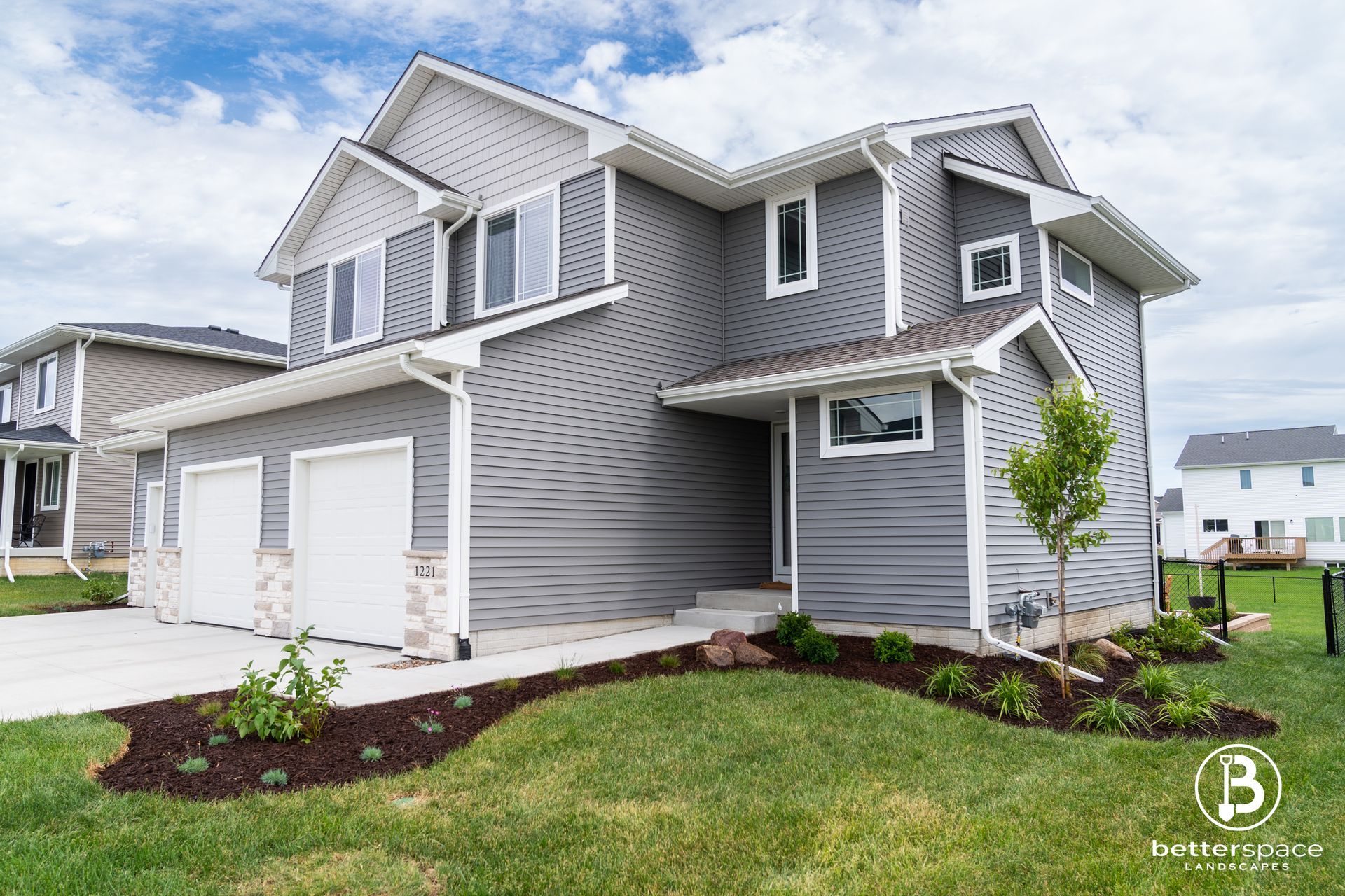 Gray two-story suburban house with white trim, two-car garage, and landscaped front yard