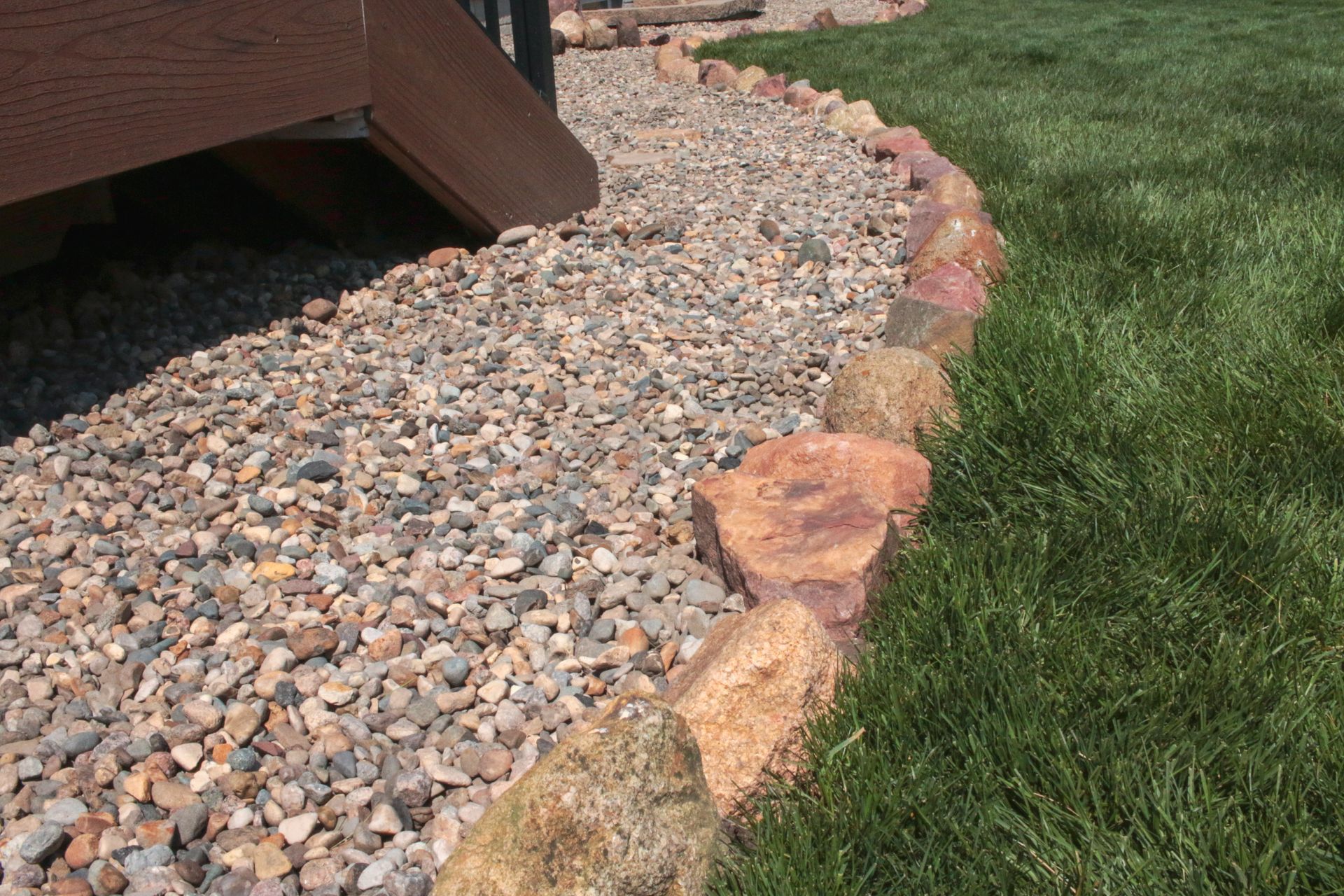 Rock border edging a gravel path beside green grass and a wooden structure.