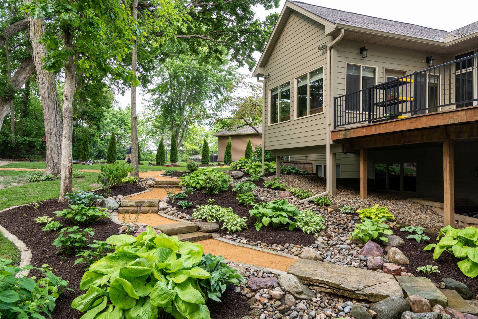 Landscaped garden with stone path and lush green plants beside a house with a raised deck