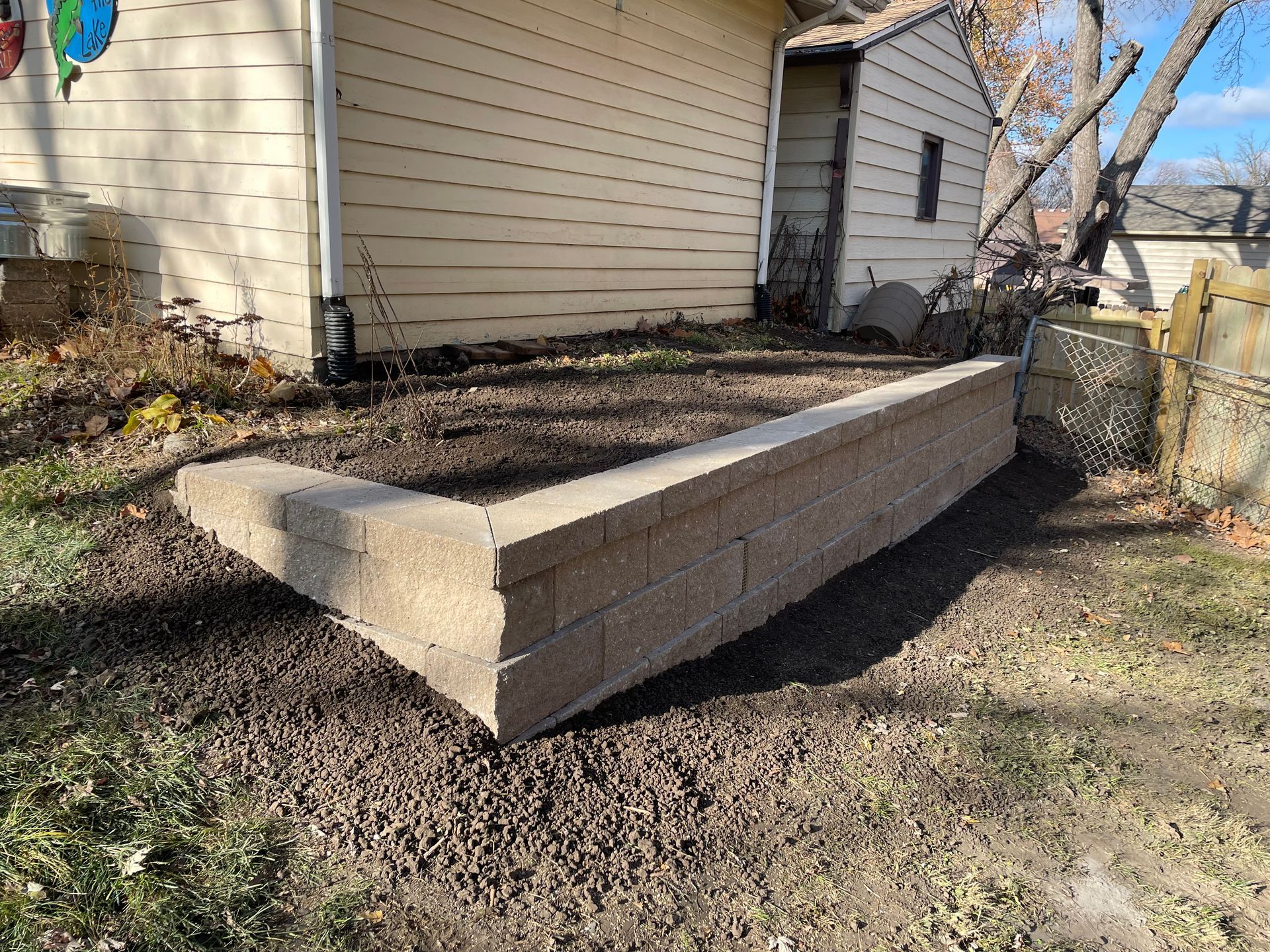 Raised wooden garden bed beside a house in a backyard, with bare soil and mulch around it.