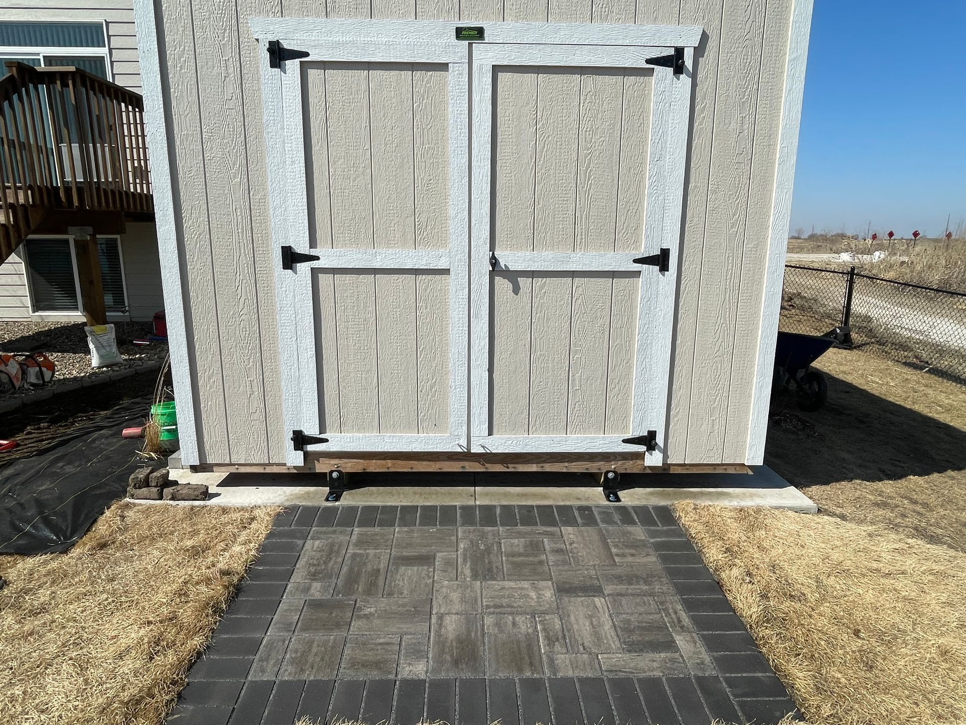 Outdoor shed with white double doors and a paved stone path leading to it