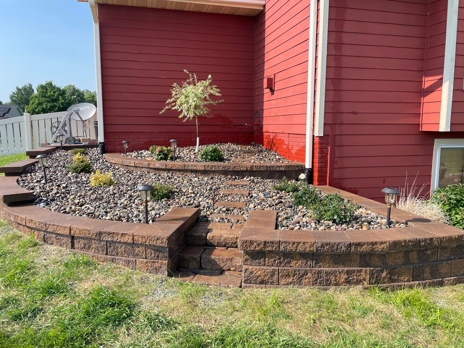 Red house exterior with raised stone landscaping beds and a small shrub in front