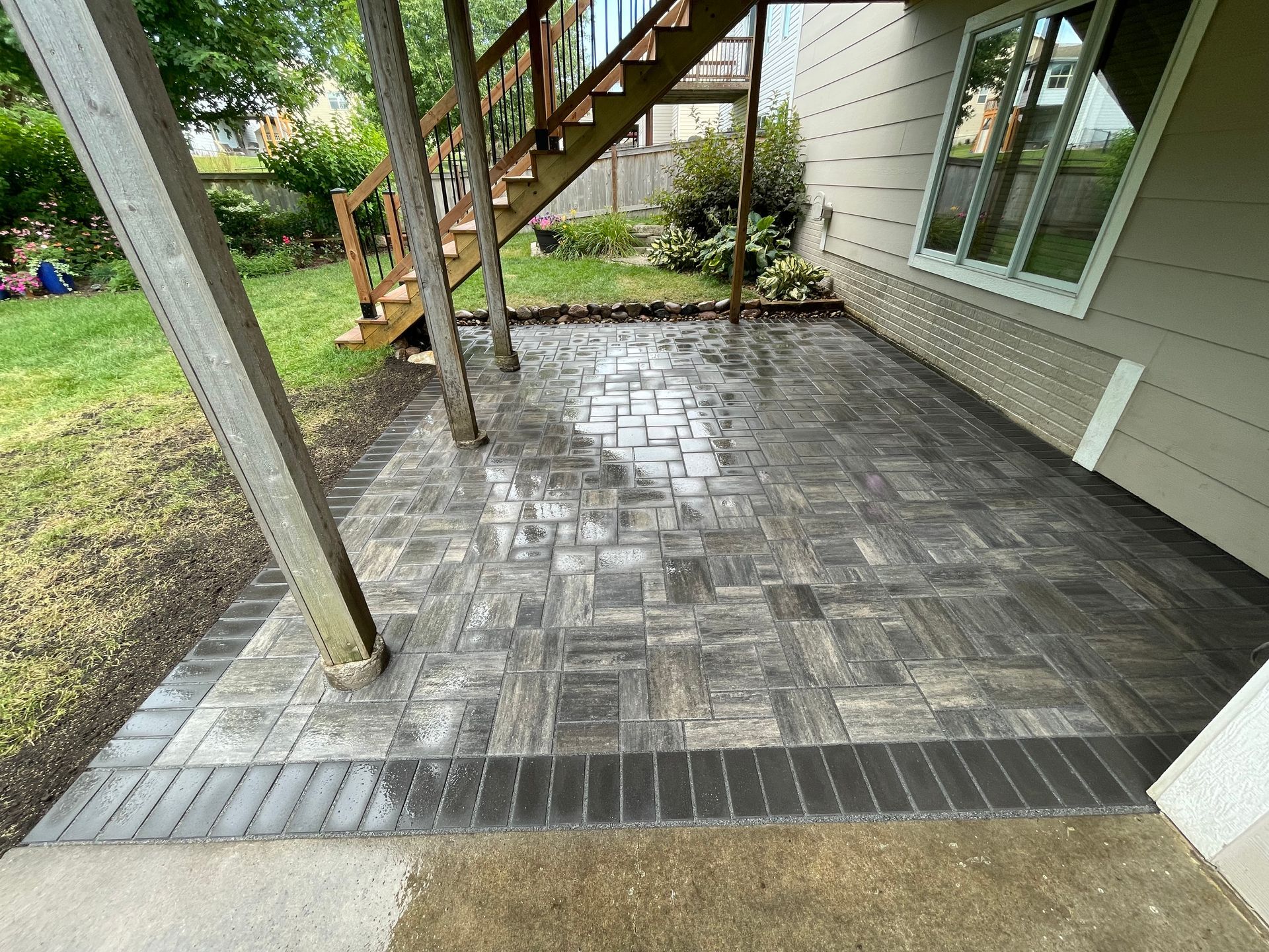 Wet patio with gray pavers under an exterior staircase beside a house