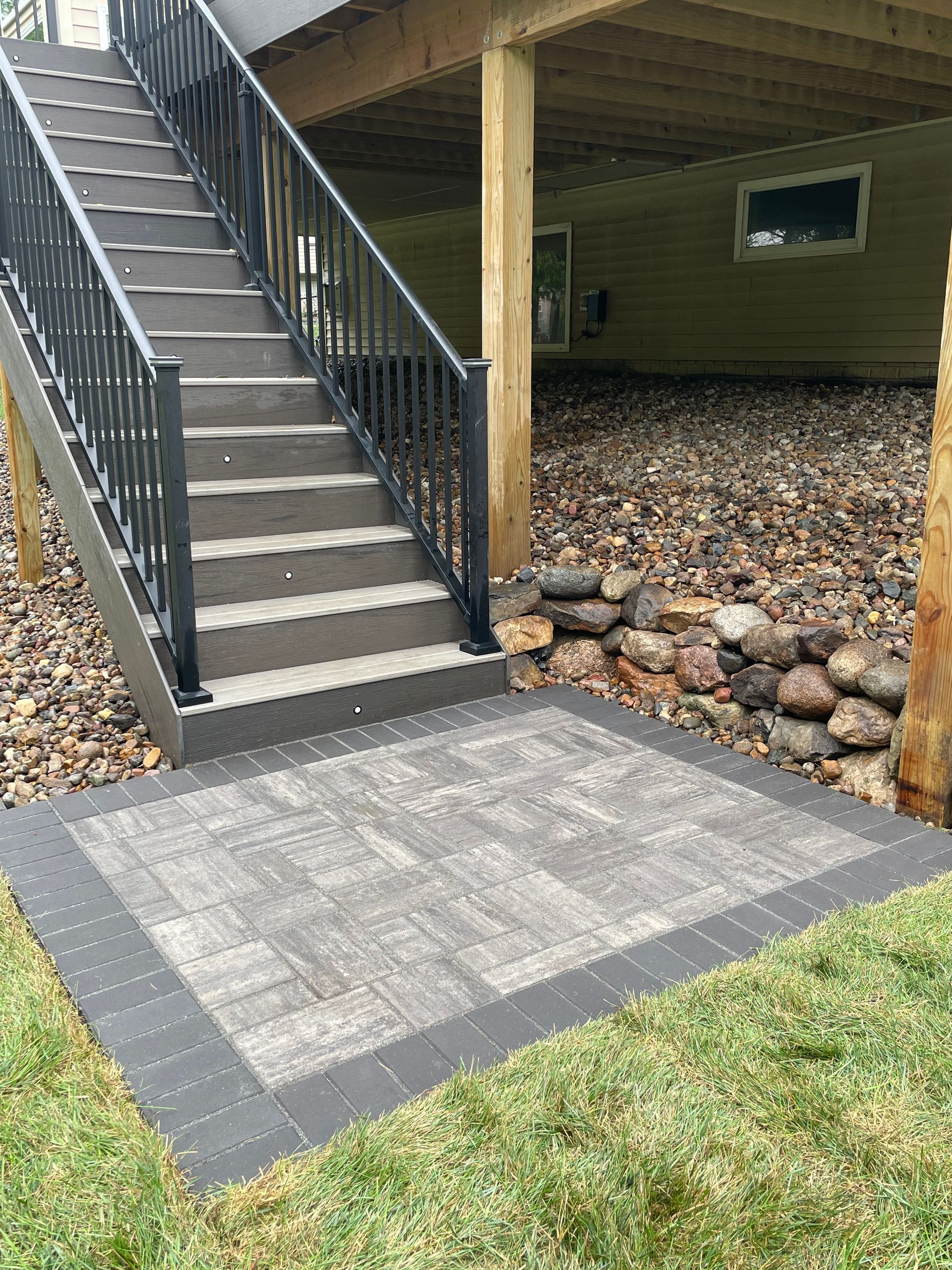 Exterior stairway with black railings beside a building, leading to a paved landing and gravel area.