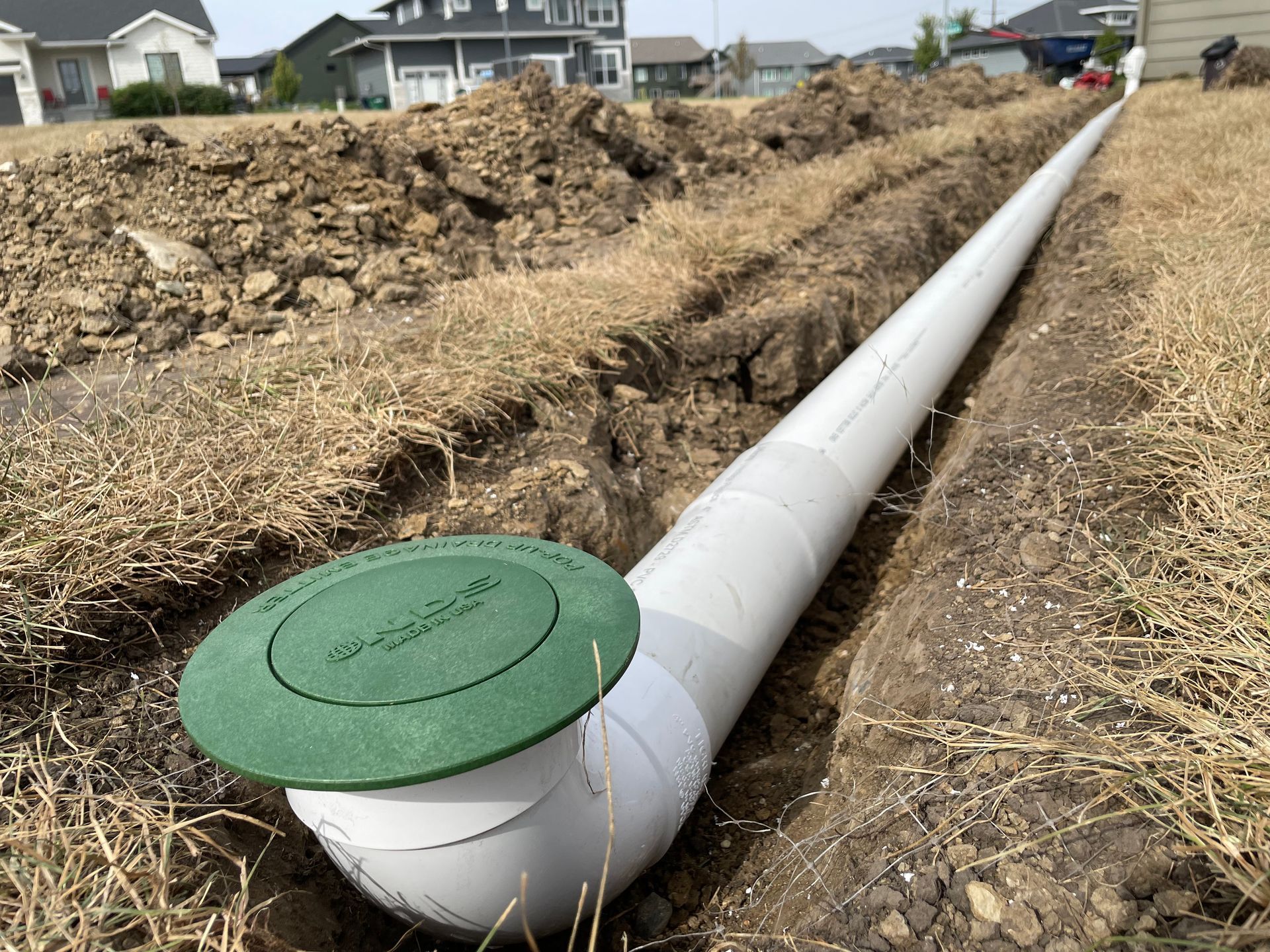 White utility pipe with green cap running through a trench in a residential area