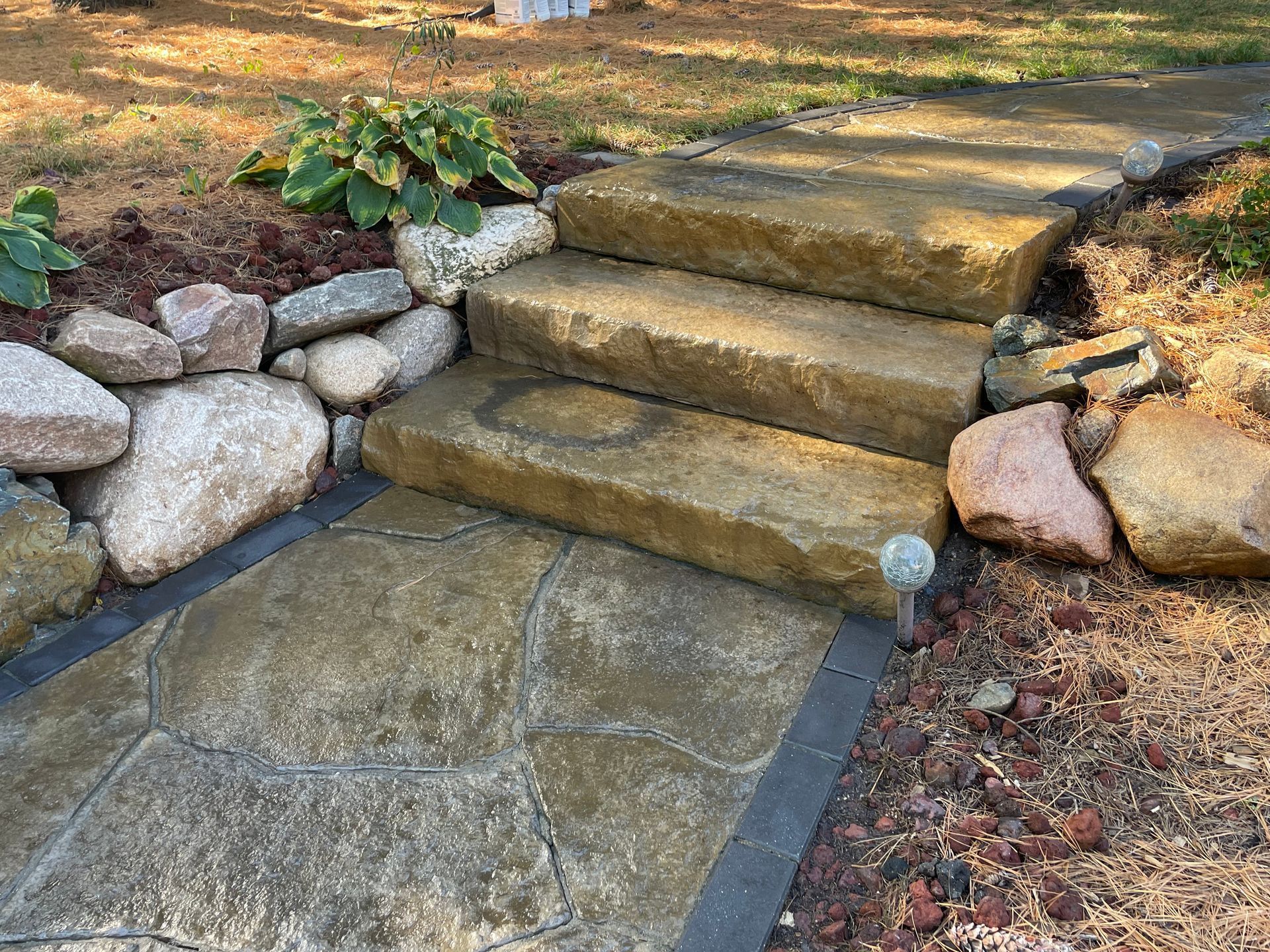 Stone steps leading up a garden path beside a rock border and dry ground