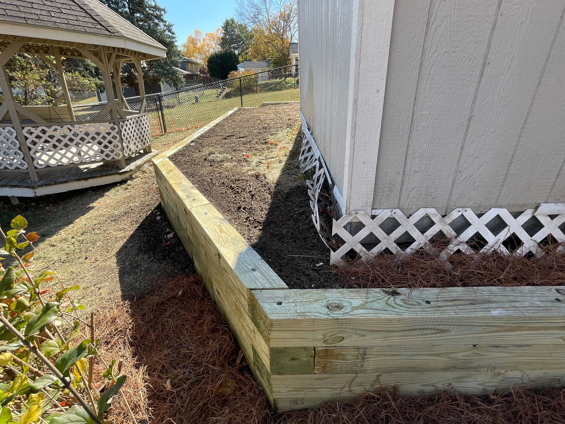 Wooden retaining wall beside a white house, with a gazebo in the background.