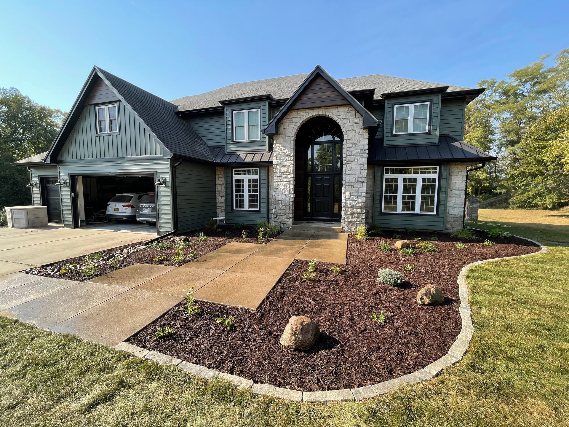 Large gray house with arched entry, attached garage, and landscaped front yard under a blue sky