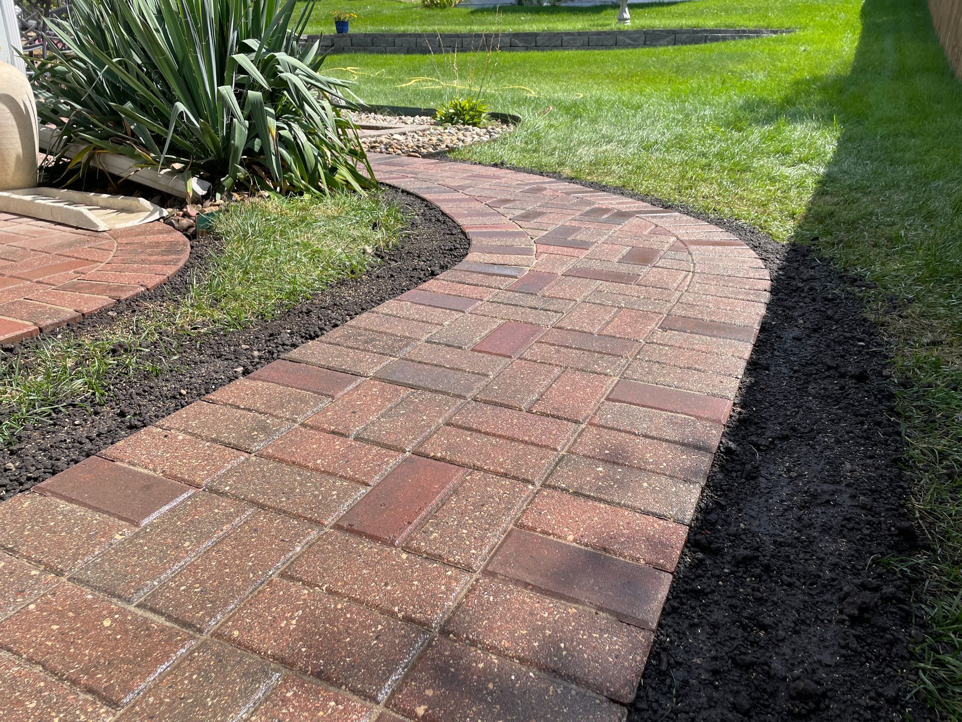 Curved brick garden pathway beside green lawn and shrubs in daylight