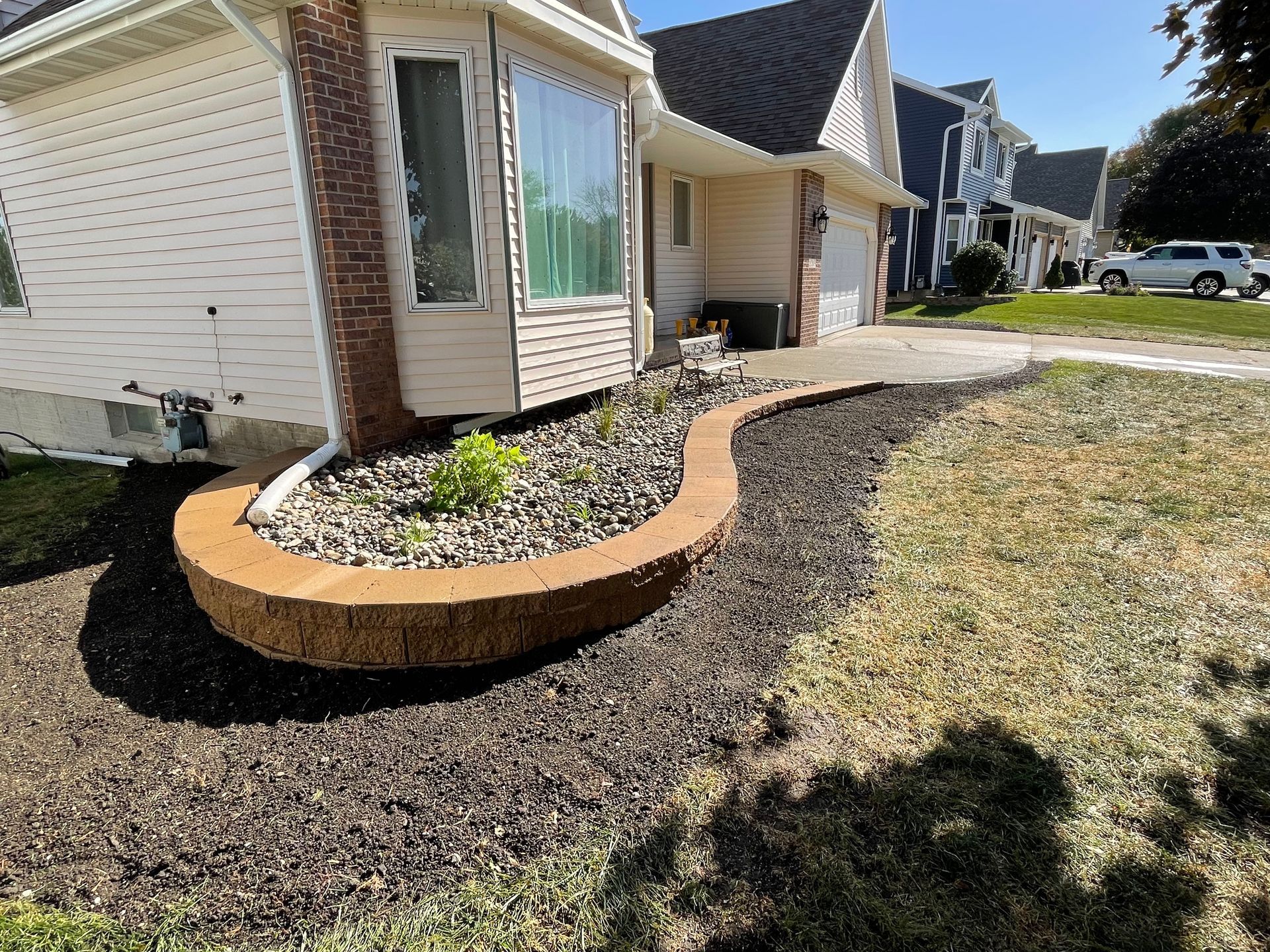 Front yard landscaping with curved mulch beds and a stone-edged planter beside a beige house
