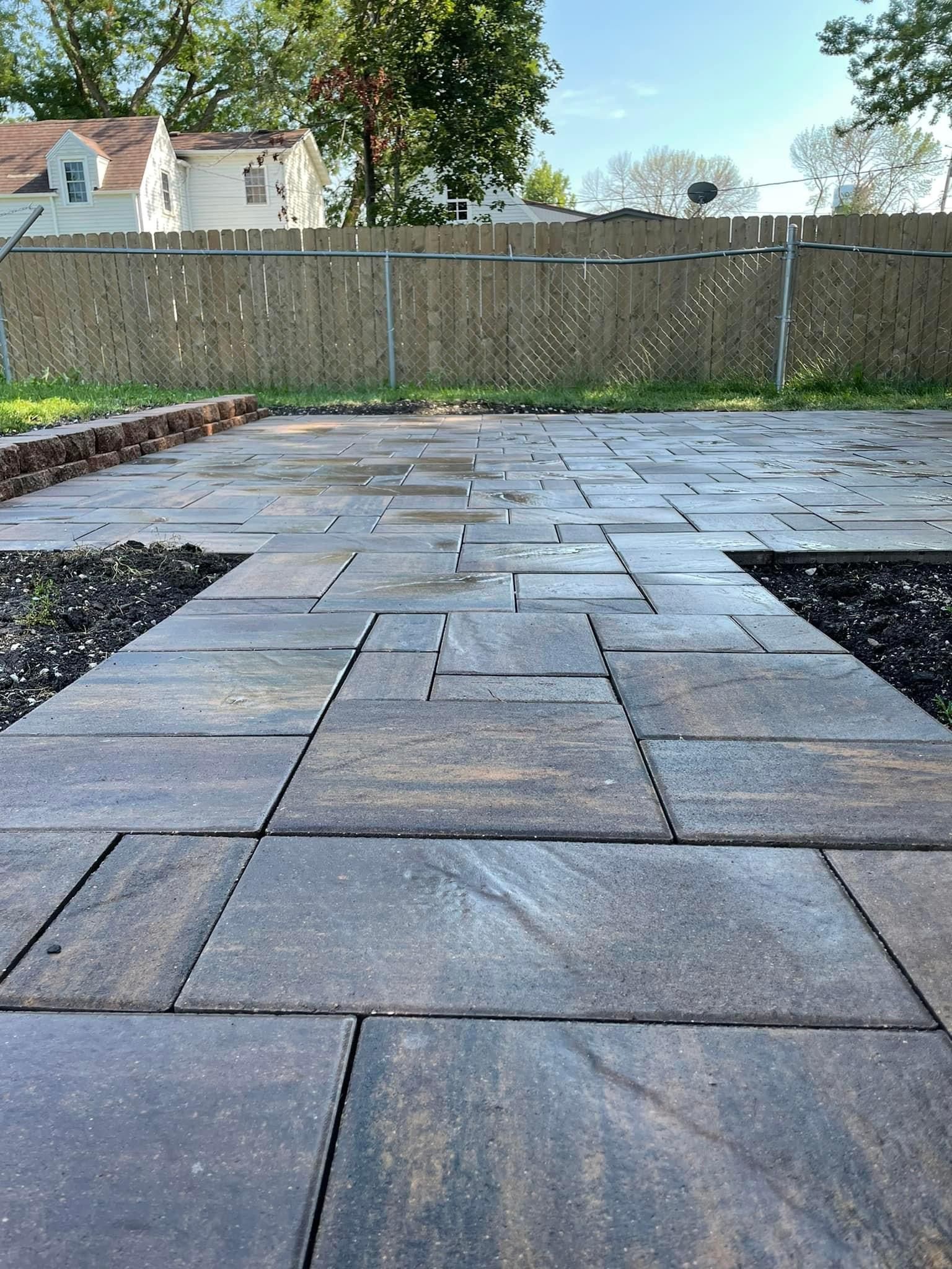 Paver stone patio leading to a wooden fence and yard, with trees and houses in the background