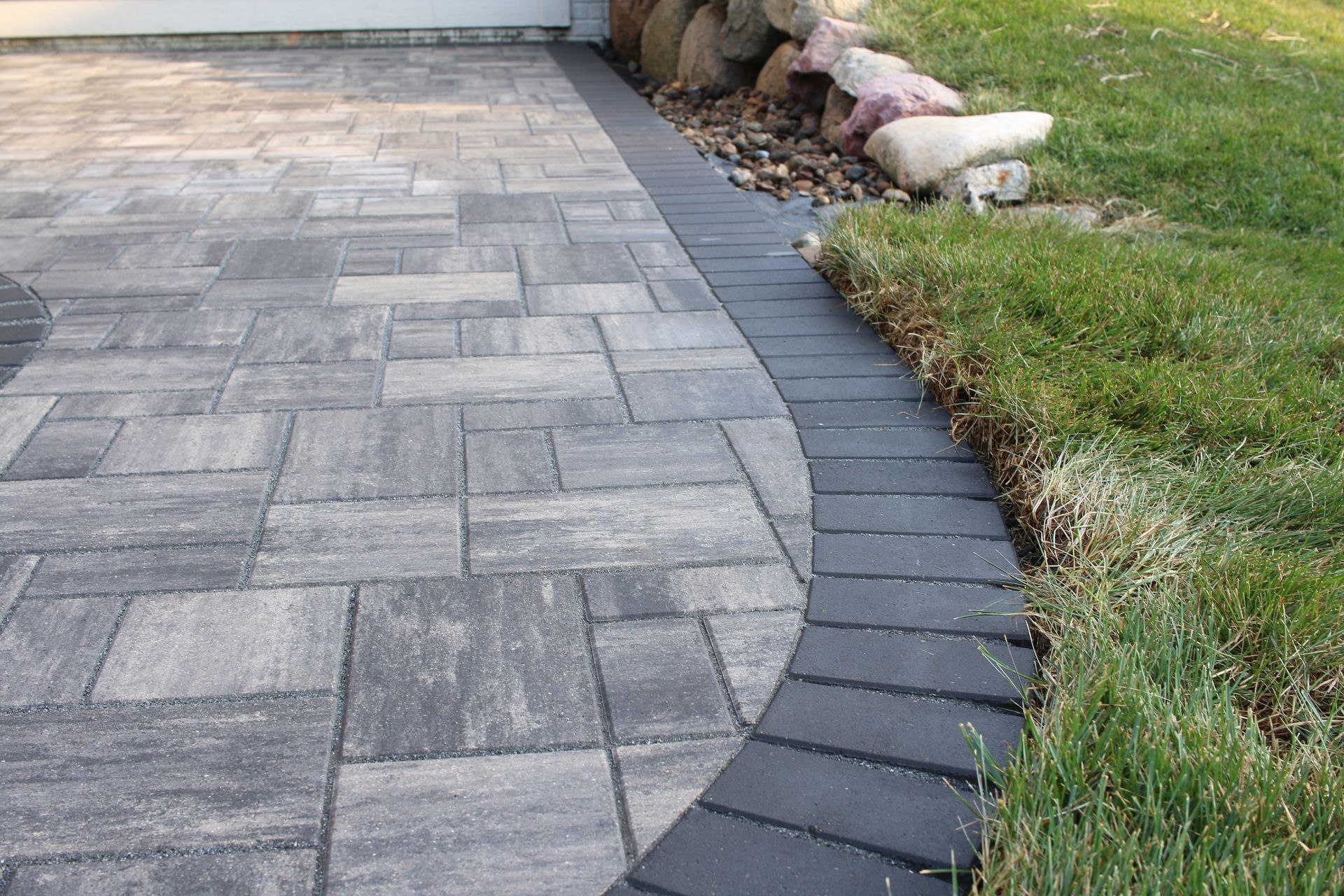 Curved paver walkway beside a lawn, bordered by dark edging and a small decorative dog statue.