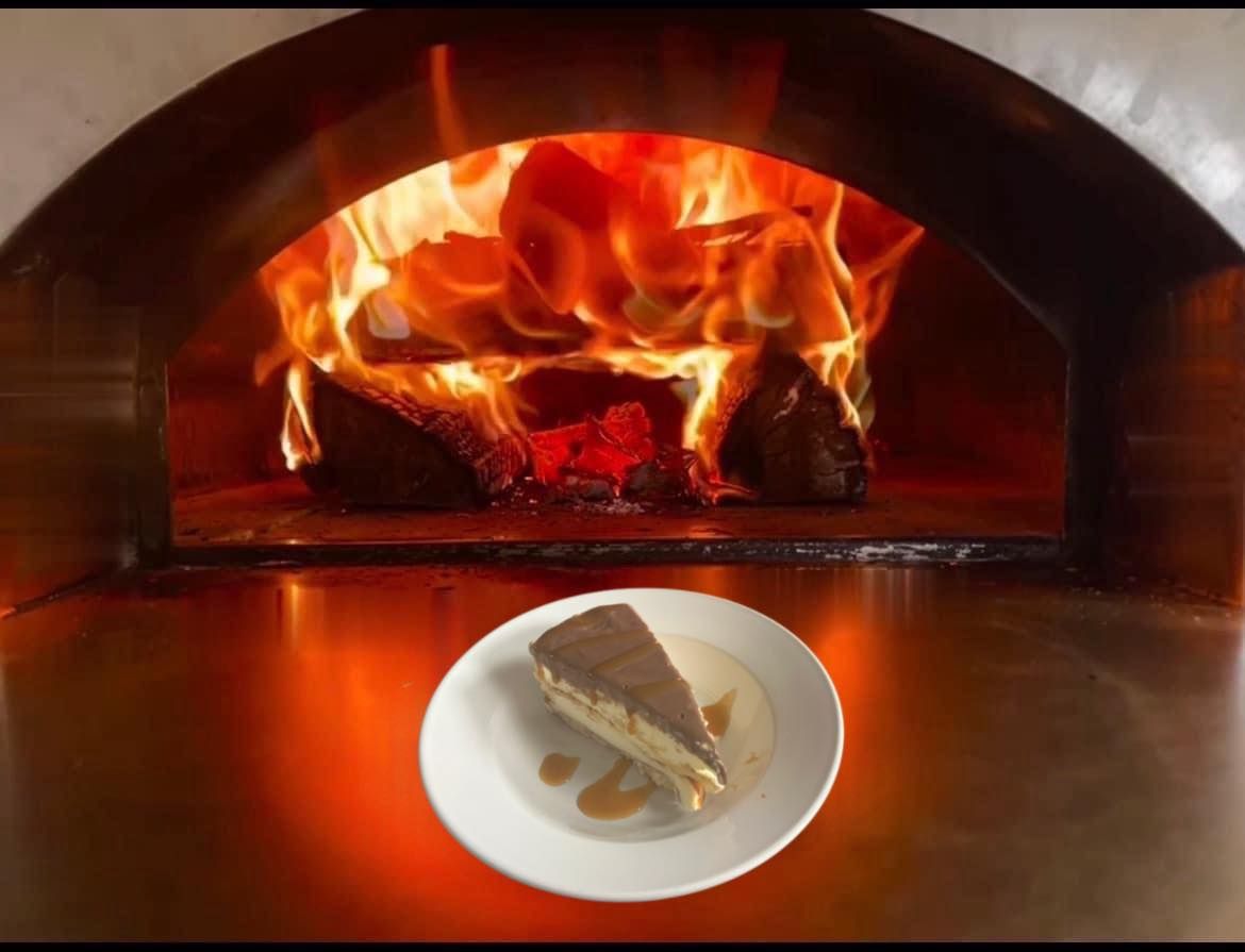 A slice of cheesecake is on a plate in front of a pizza oven.