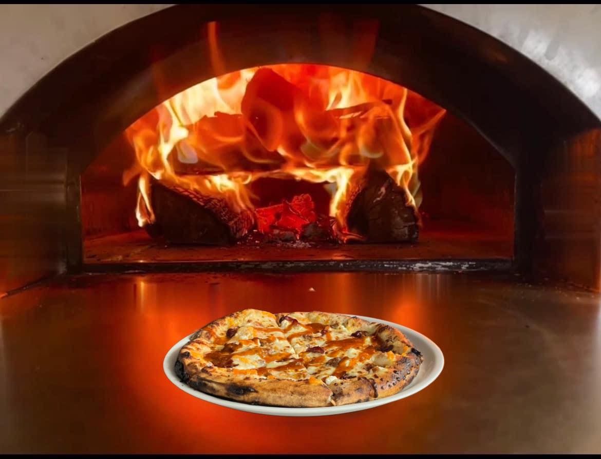 A pizza is sitting on a plate in front of a pizza oven.