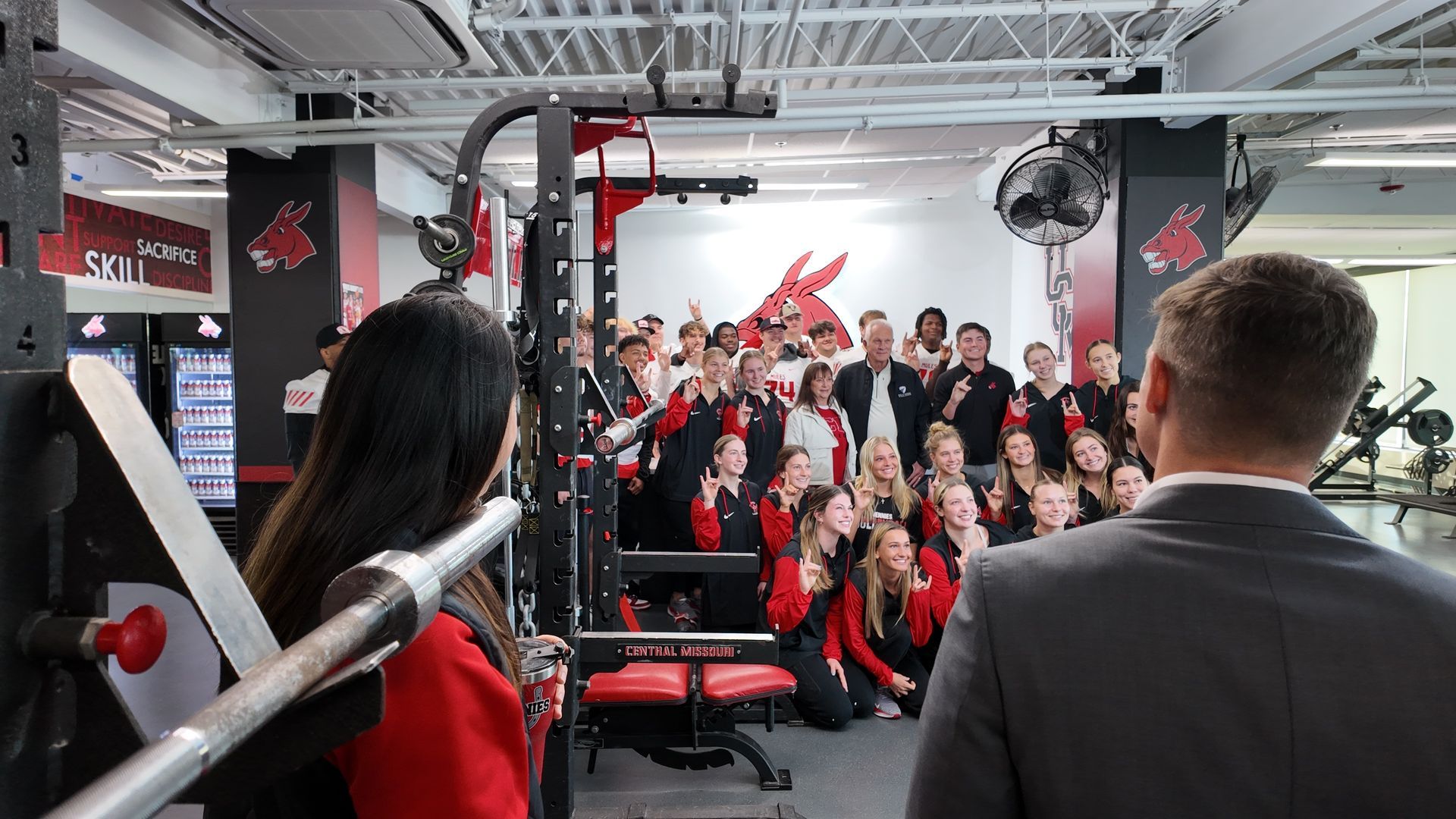 People posing in UCM school colors in a gym, cheering toward the camera
