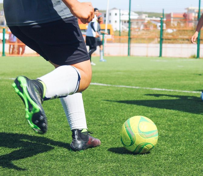 A soccer player in dark shorts and white socks prepares to kick a lime green and yellow ball on a turf field.