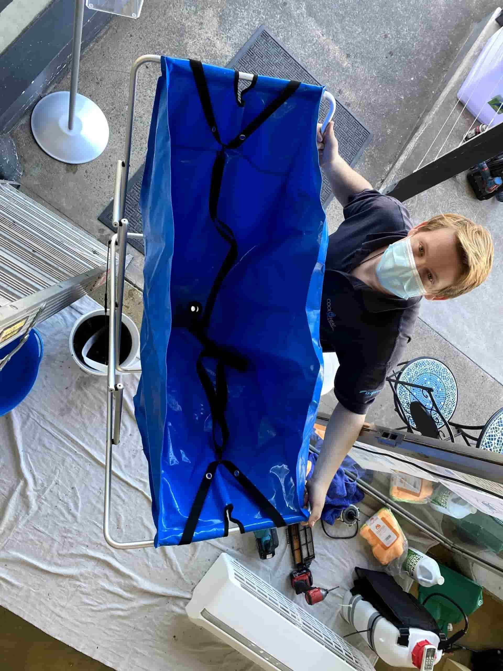 A Man Wearing a Mask is Working With a Blue Bag — Cool Heat Air Conditioning in Albion Park, NSW