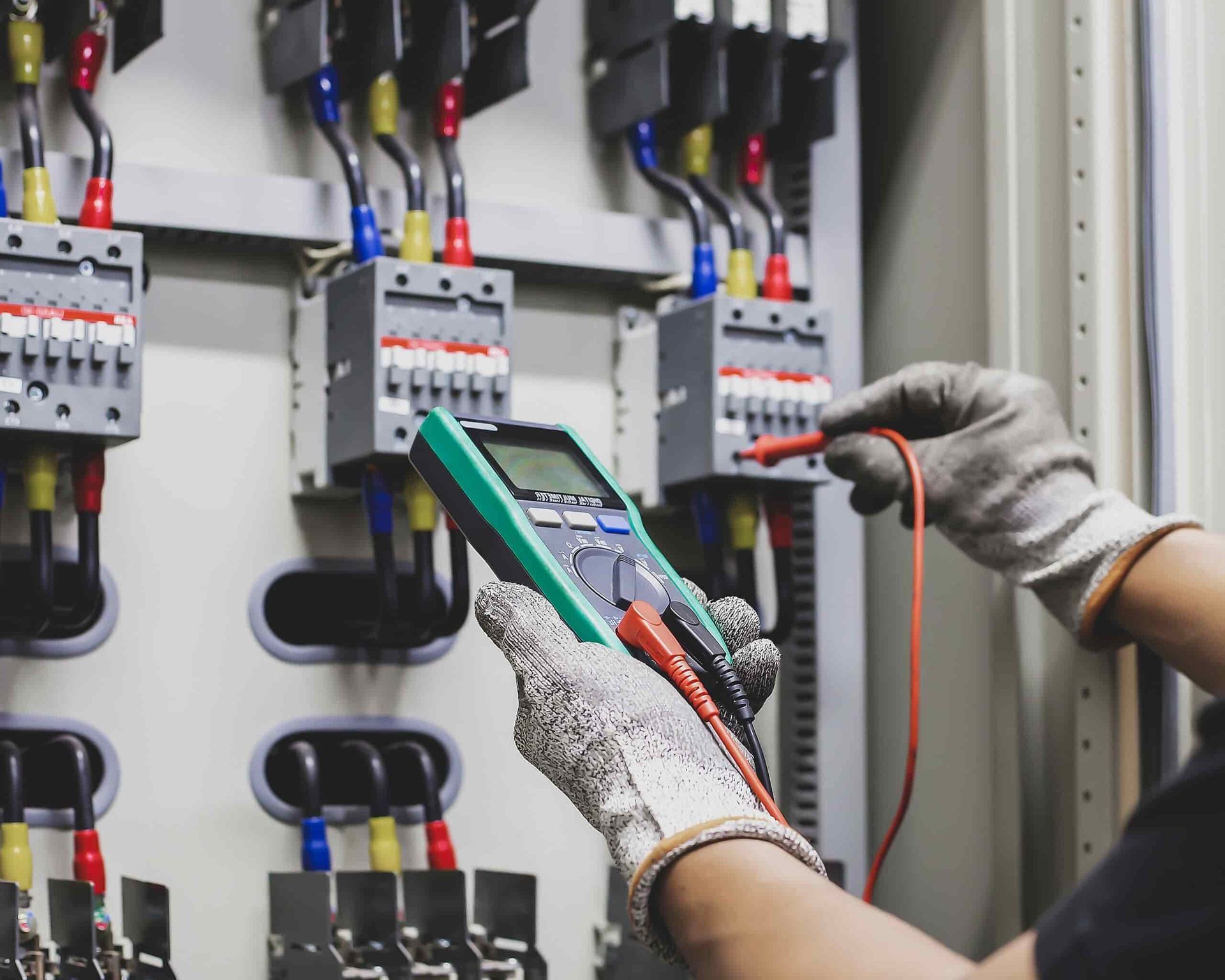A Person is Holding a Multimeter in Front of an Electrical Panel — Cool Heat Air Conditioning in Albion Park, NSW