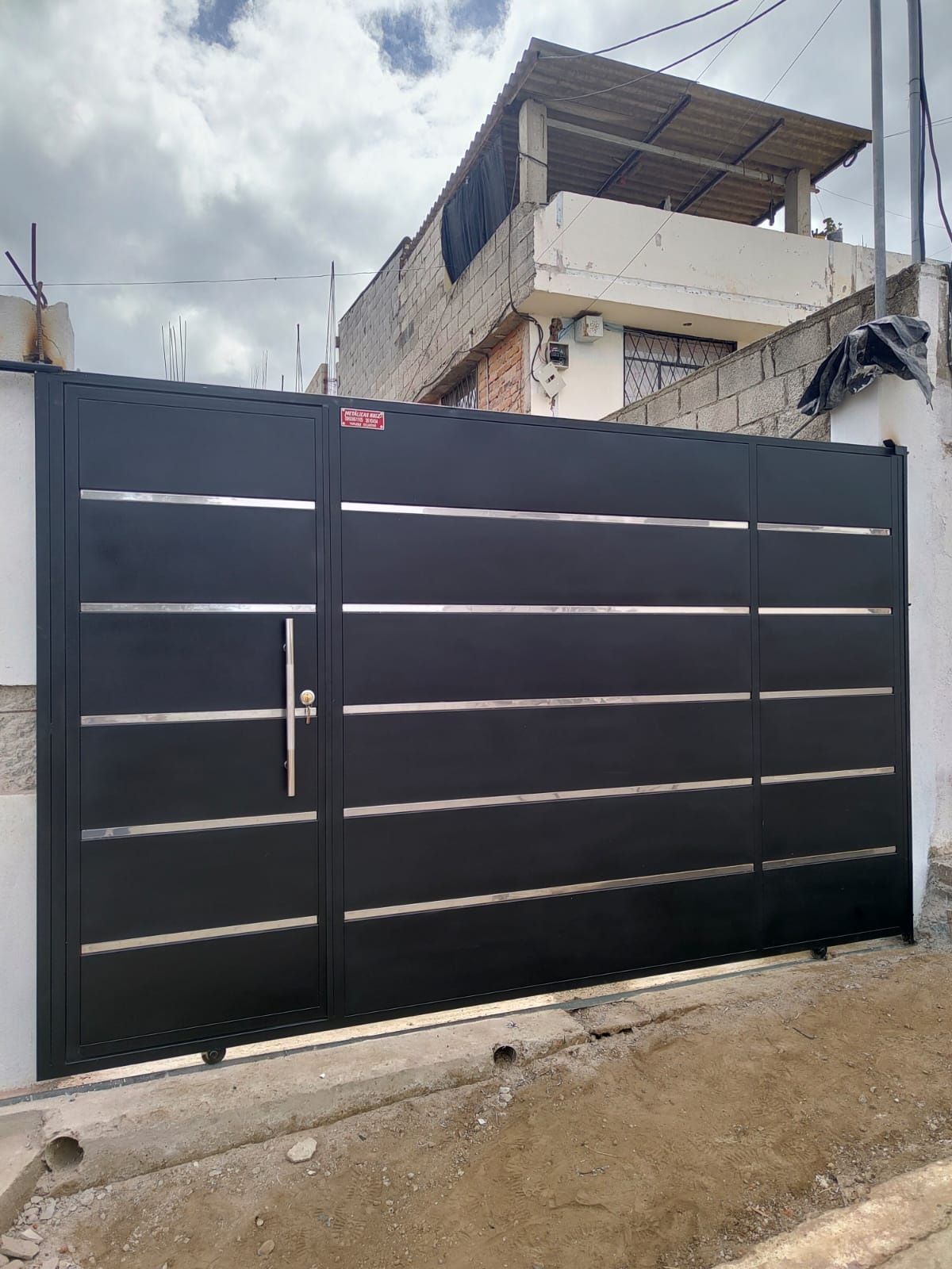 Una puerta corredera negra con tiras horizontales de metal plateado y una manilla vertical alta