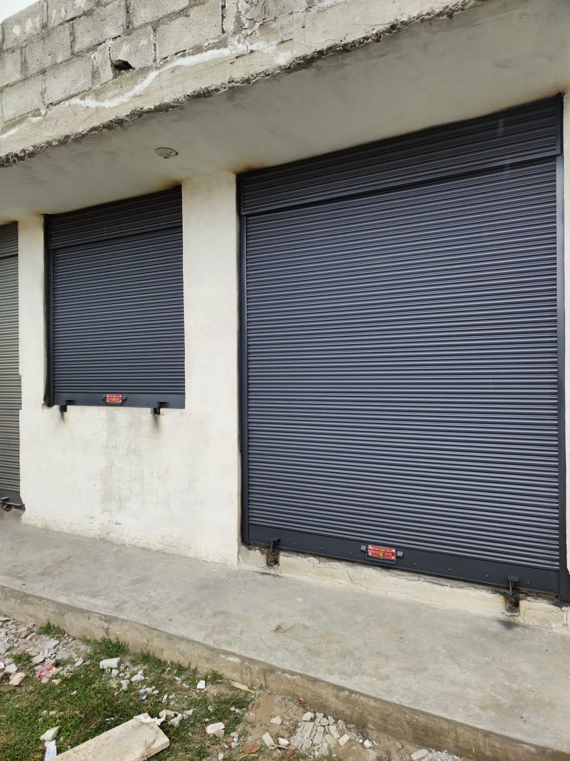 Un edificio de color blanco con dos puertas de seguridad enrollables de metal gris oscuro cerradas