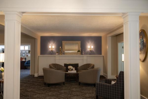 Elegant lobby with gray chairs, purple walls, and a lit fireplace beneath a large mirror