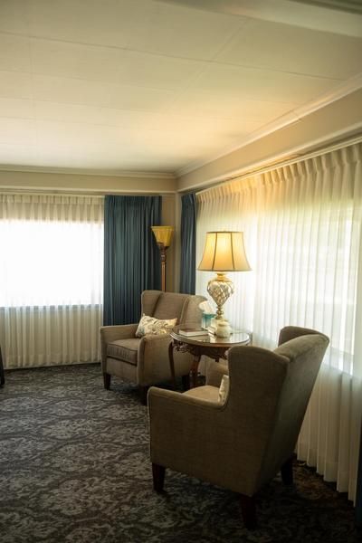 Living room with beige chairs, table lamp, curtains, and patterned carpet in soft light