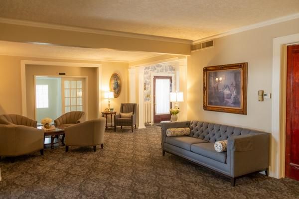 Spacious beige living room with a gray sofa, chairs, carpeted floor, and large wall art.