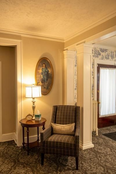 Elegant hallway with armchair, side table lamp, and framed wall art near a doorway