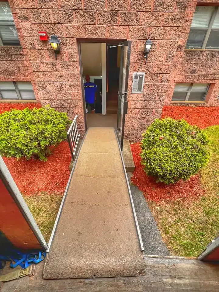 Brick apartment entrance with a narrow concrete ramp leading to an open doorway